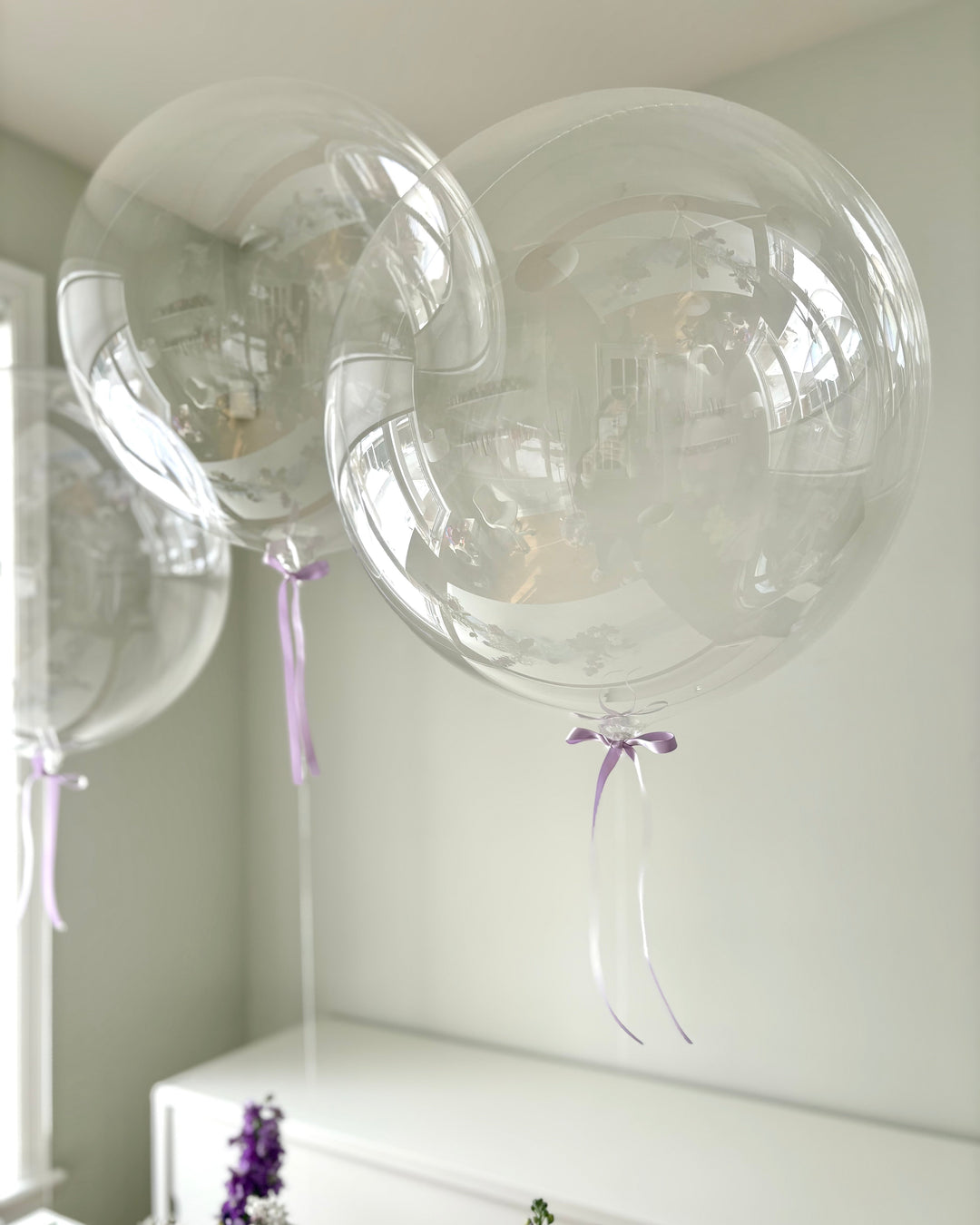 Clear balloons with purple bows on a white surface