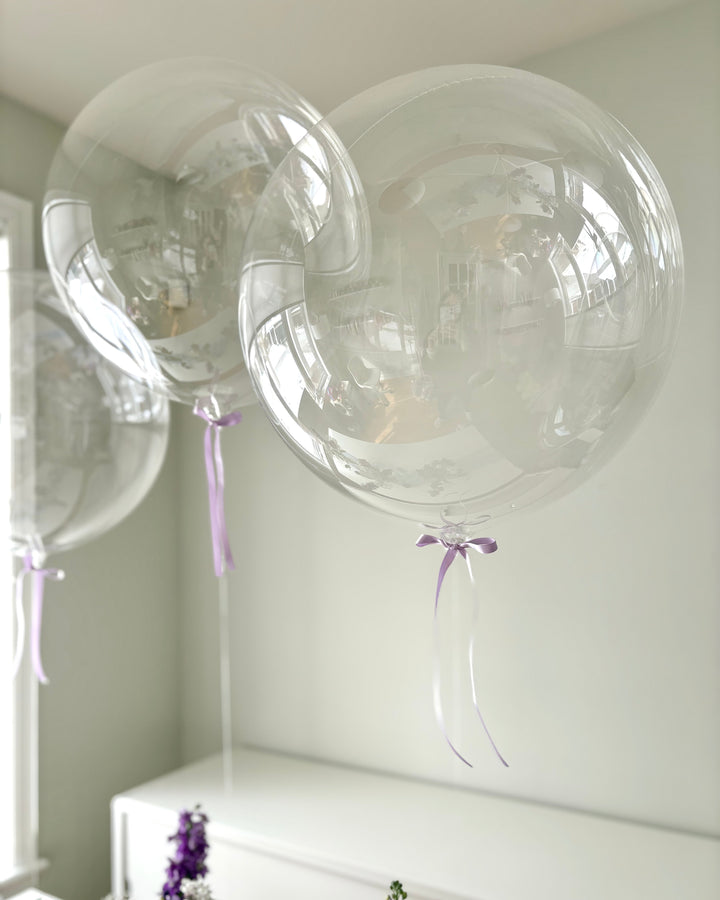 Clear balloons with purple bows on a white surface
