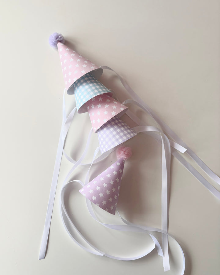 four birthday party hats stacked together on their sides, and a party hat on its own near the other 4, on a flat white surface