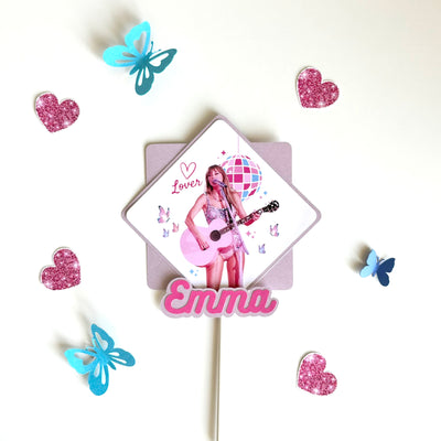 cake topper in Taylor Swift lover theme, square image with taylor swift singing with guitar and disco ball and butterflies with the word "lover" and a heart, mounted on lilac shimmer card stock and name in pink and purple shimmer backing