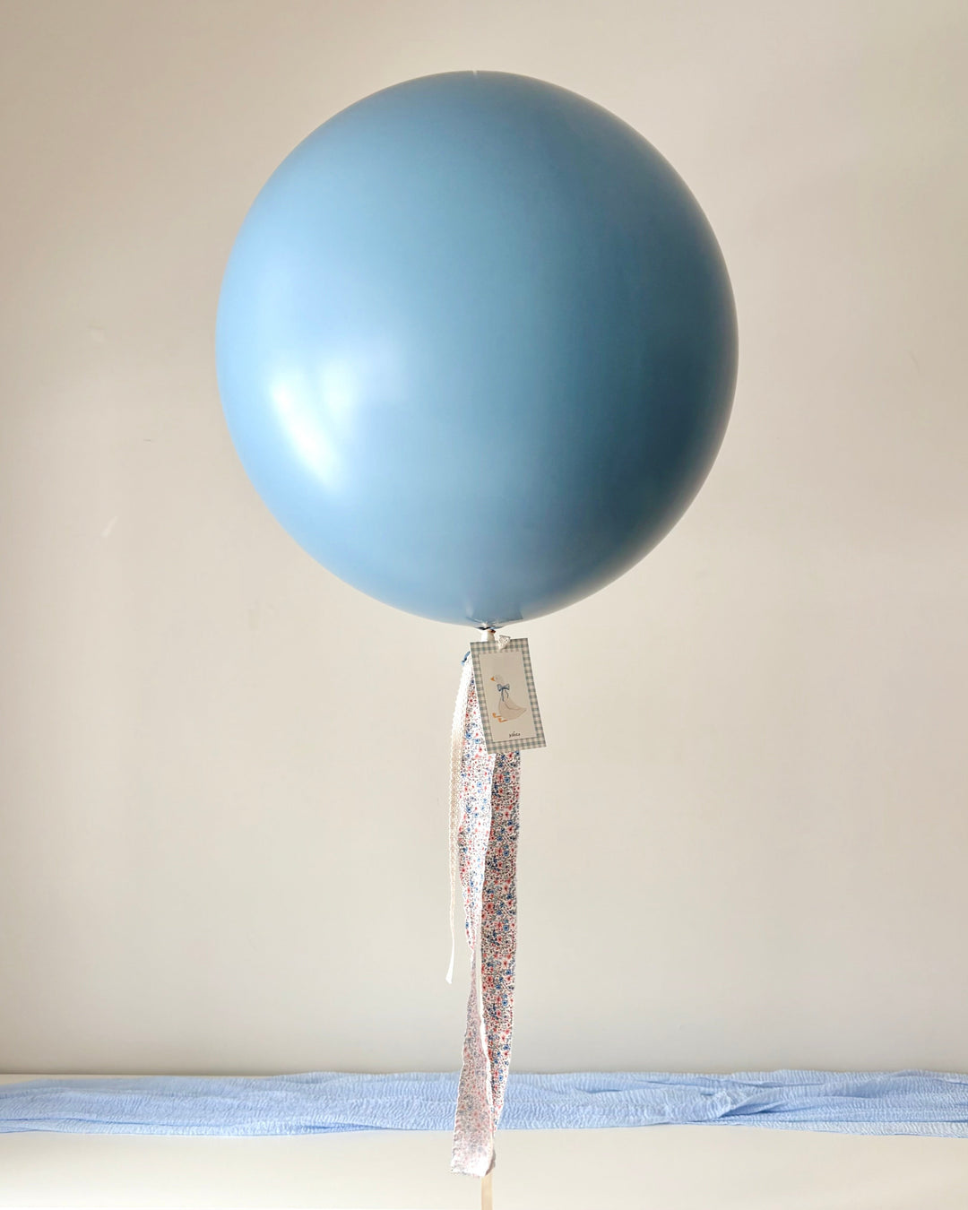 Blue jumbo latex balloon with a fabric floral and lace tassel and a paper card with a silly goose print