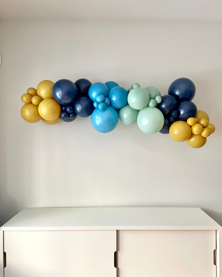 Colorful balloon garland against a white wall with a white cabinet below.
