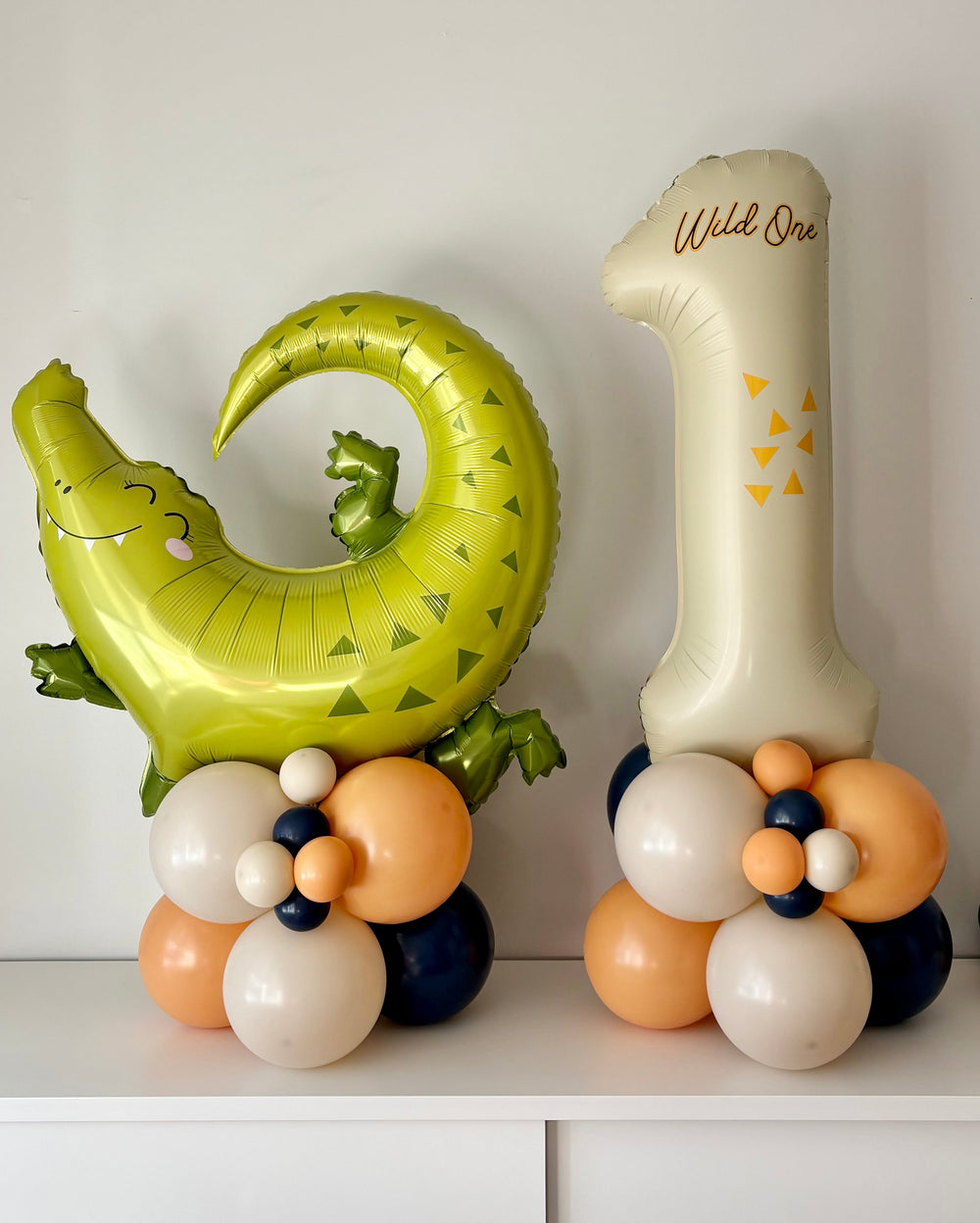 set with alligator balloon column and number 1 balloon column with the text "wild one" on a side table in a room