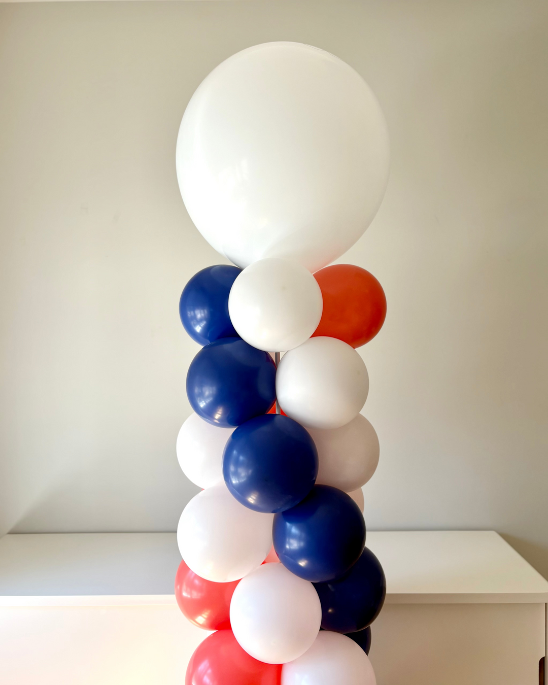 Close up of a balloon column with red, white, and blue balloons, in a room with a sideboard in the background