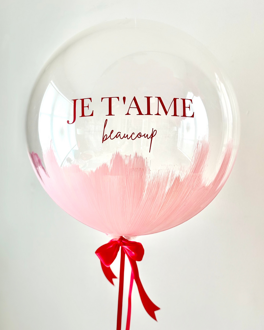 close up of bubble balloon with the text "JE T'AIME beaucoup" and satin bow