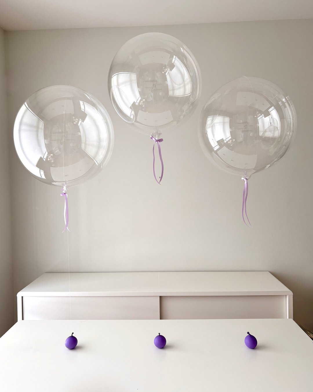 Clear balloons with satin bows floating above a white table with balloon weights