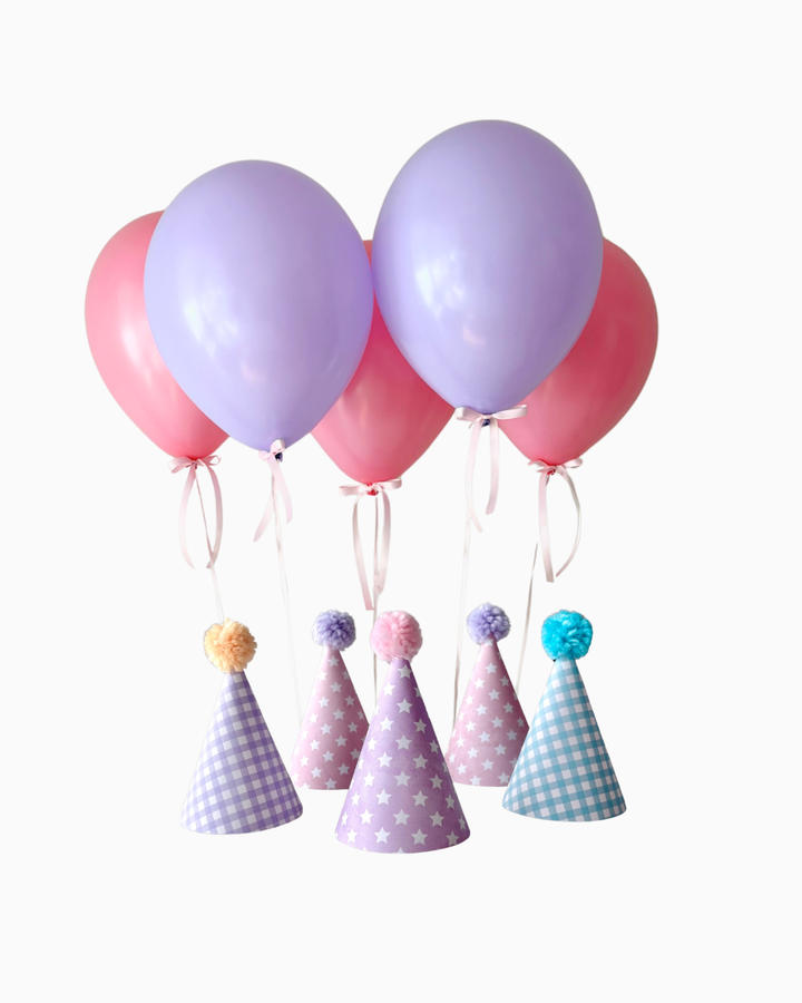 Pink and purple balloons with colorful party hats with pom poms on a white background
