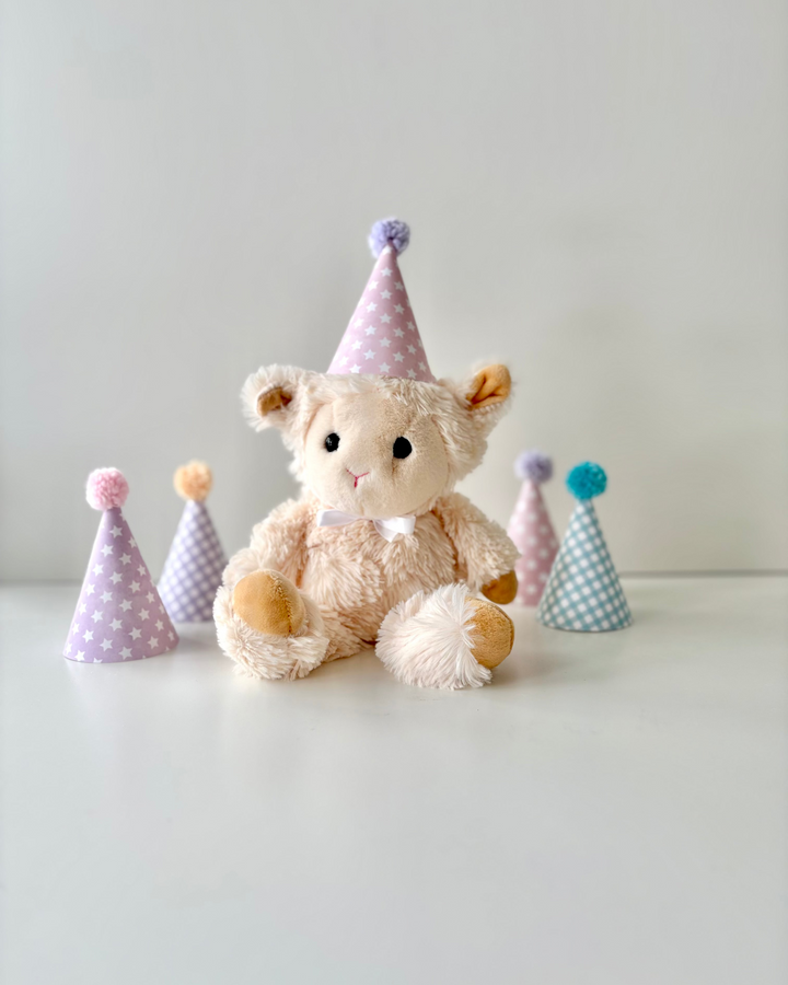 Stuffed bear wearing a party hat with small party hats around it on a light background