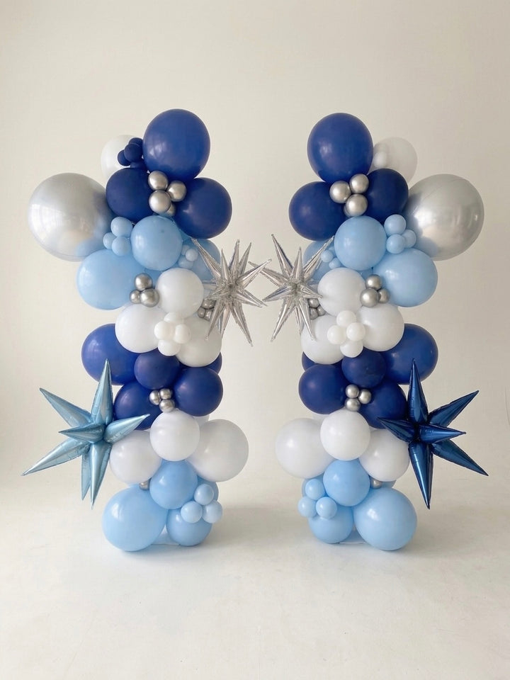 pair of organic balloon column arrangement with metallic star shaped 3D balloons starbursts and orbz (sphere) balloon, studio setting with plain white photographer backdrop