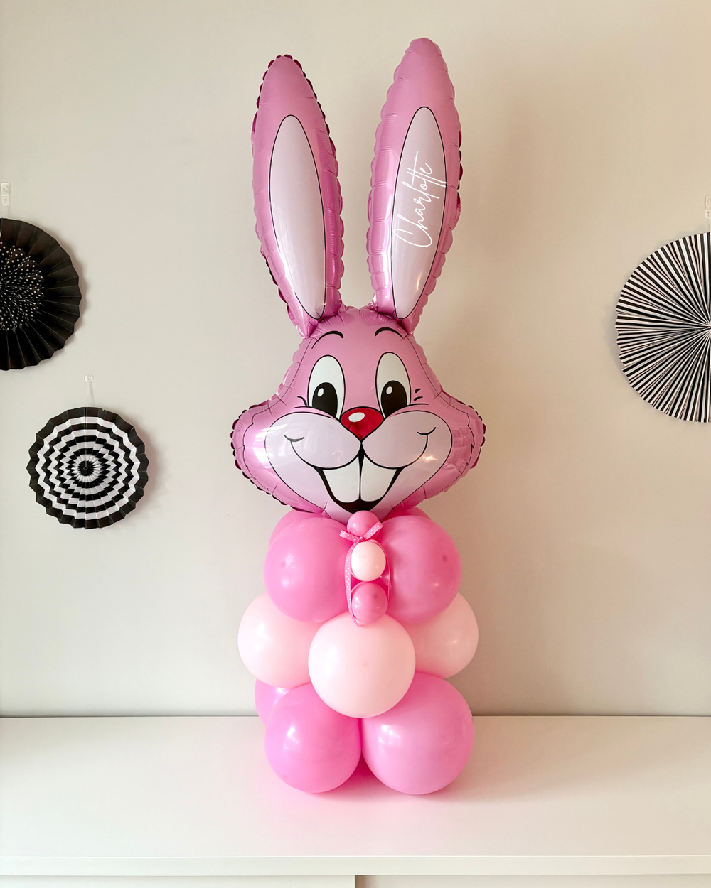 A pink balloon column featuring a jumbo bunny head balloon with custom text, on a side table