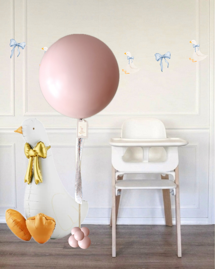 pink jumbo balloon next to a white high chair and a sitting goose balloon in a room